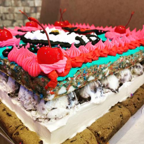 A colorful layered cake topped with pink frosting, cherries, and decorative icing, featuring a fun design.