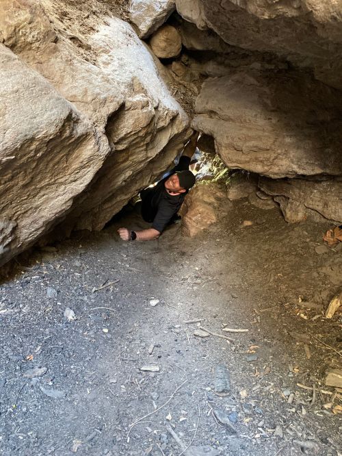 A person crawling through a narrow space between large rocks in a natural setting.