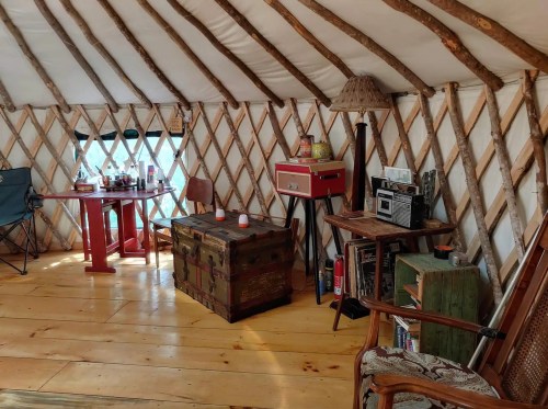 Cozy interior of a yurt featuring wooden beams, a table, chairs, a trunk, and various decor items.