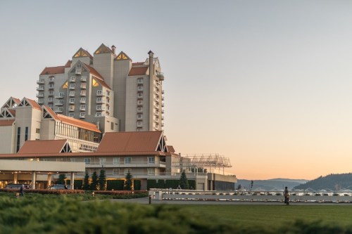 A large hotel with a distinctive architectural design, set against a sunset sky and surrounded by greenery.