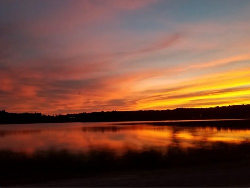 A vibrant sunset over a calm lake, with orange and pink hues reflecting on the water's surface.