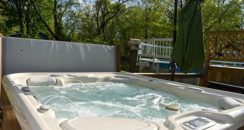 A hot tub filled with bubbling water, surrounded by greenery and a sunny outdoor setting.