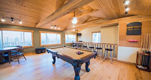 A spacious game room with a pool table, bar stools, and large windows overlooking a scenic view.