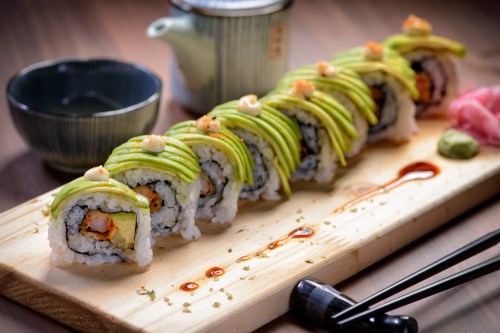 A beautifully arranged sushi roll topped with avocado, served on a wooden platter with soy sauce and wasabi.