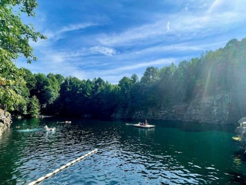 A serene lake surrounded by trees, with people kayaking and a clear blue sky above.