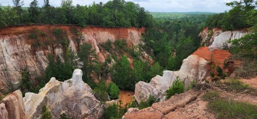 A scenic view of a deep canyon with red and white cliffs, surrounded by lush green trees under a cloudy sky.