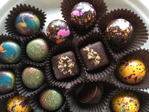 A variety of colorful, artistic chocolates arranged in dark paper cups on a white plate.