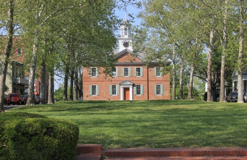 A historic brick building with a clock tower, surrounded by green trees and a lawn.