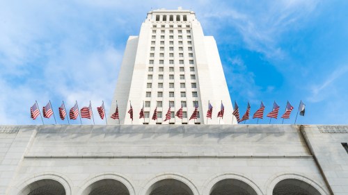 A tall building with a clock tower, adorned with multiple American flags against a blue sky.