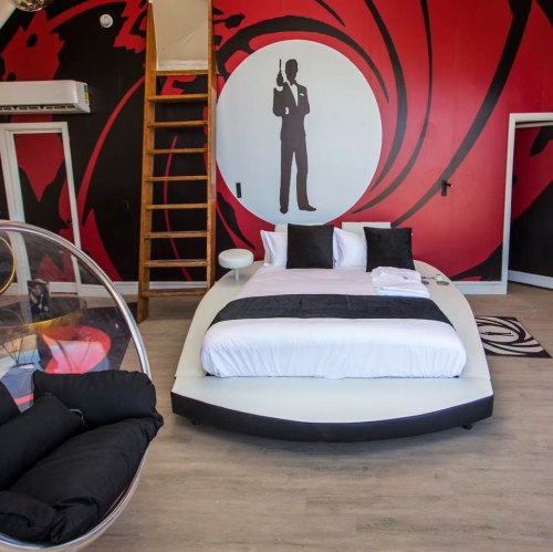 A modern bedroom featuring a round bed, black and white decor, and a large mural of a suited figure on a red wall.
