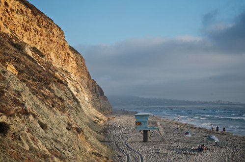 A sandy beach with a lifeguard tower, cliffs in the background, and a few people enjoying the shoreline.