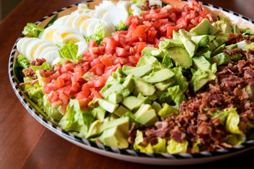 A colorful salad platter with chopped lettuce, tomatoes, avocado, bacon, and sliced hard-boiled eggs.