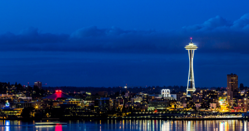 Seattle skyline at dusk, featuring the illuminated Space Needle and reflections on the water.