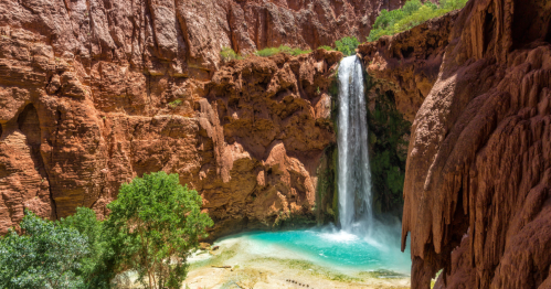 A stunning waterfall cascades into a turquoise pool, surrounded by red rock formations and lush greenery.