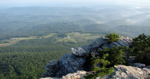 A panoramic view from a rocky outcrop, overlooking lush green hills and valleys under a clear sky.