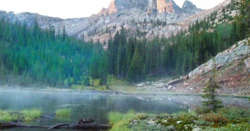 Serene mountain landscape with a misty lake, surrounded by lush greenery and towering peaks in the background.