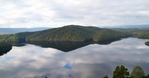 A serene lake surrounded by lush green hills, reflecting the cloudy sky above.