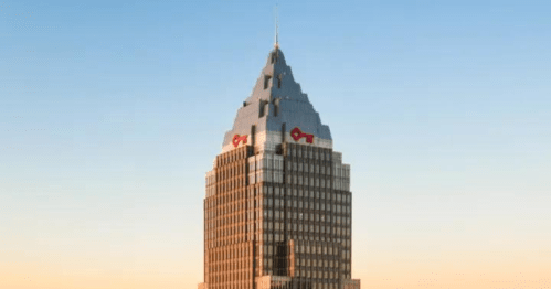 A tall, modern skyscraper with a distinctive peaked roof against a clear blue sky.