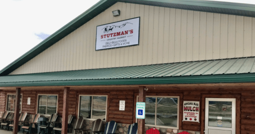 Exterior of Stutzman's Country Market, featuring a sign and wooden chairs outside a rustic building.