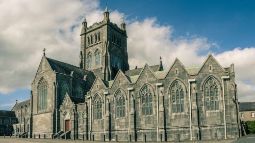 A large stone church with intricate Gothic architecture under a blue sky with clouds.