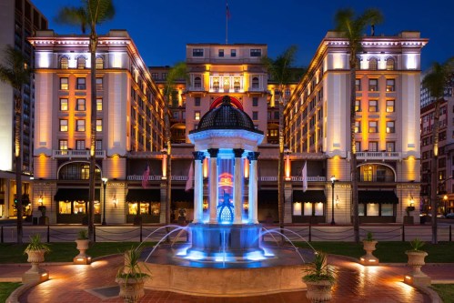 A beautifully lit hotel facade at night, featuring a colorful fountain in the foreground and palm trees.