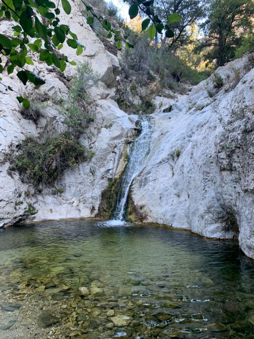A serene waterfall cascading into a clear pool, surrounded by rocky terrain and lush greenery.