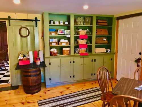 A cozy room featuring a green cabinet filled with dishes and baskets, wooden chairs, and a striped rug on the floor.