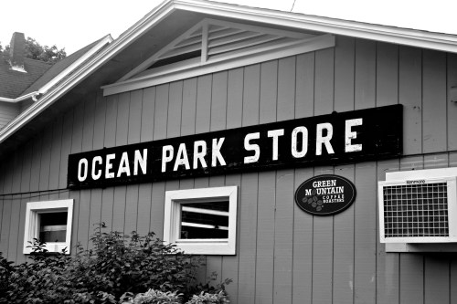 Black and white image of the Ocean Park Store sign on a wooden building, with a coffee roaster sign nearby.