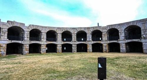 Stone structure with arched openings, surrounded by grass under a cloudy sky.