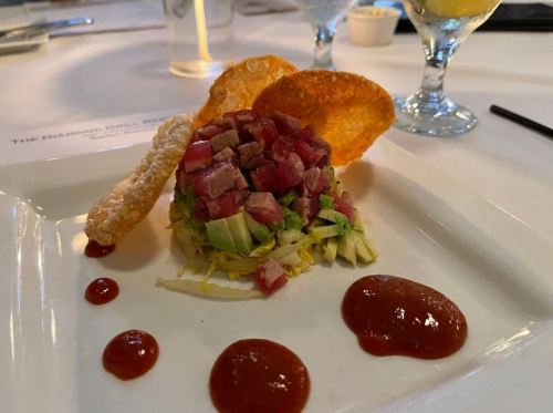 A plated dish featuring diced meat on a bed of lettuce, garnished with sauces and crispy elements on the side.