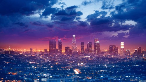 A vibrant sunset over the Los Angeles skyline, with colorful clouds and city lights illuminating the scene.