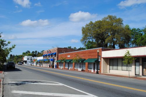 A quiet street scene featuring brick buildings, green awnings, and a clear blue sky with a few clouds.