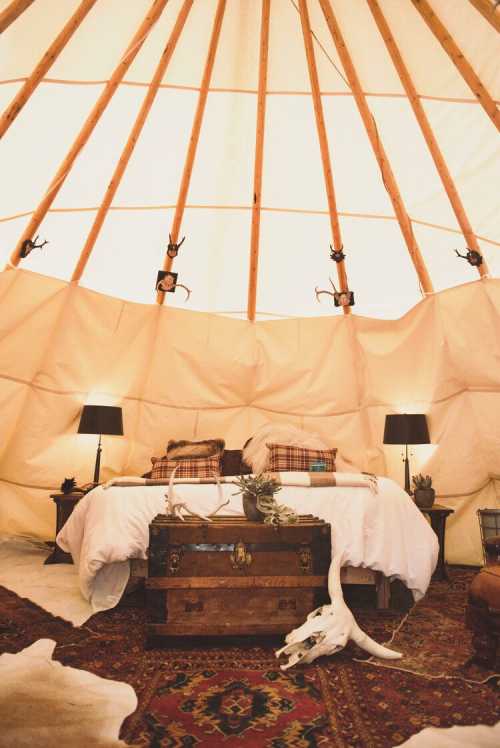 Cozy interior of a yurt with a bed, lamps, a trunk, and decorative elements like a skull and patterned rug.