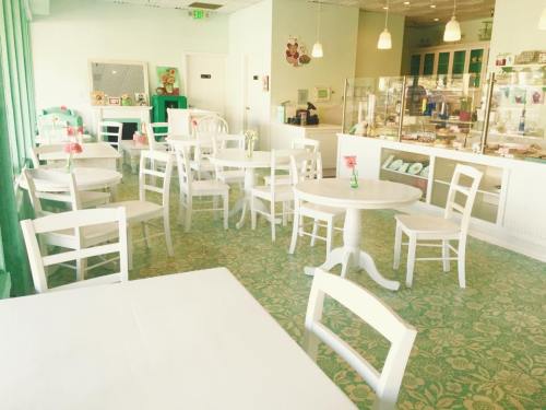 Bright café interior with white tables and chairs, green accents, and floral decorations on tables.