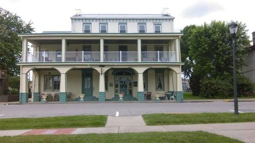 A large, two-story building with a porch, green accents, and a grassy area in front, set against a cloudy sky.