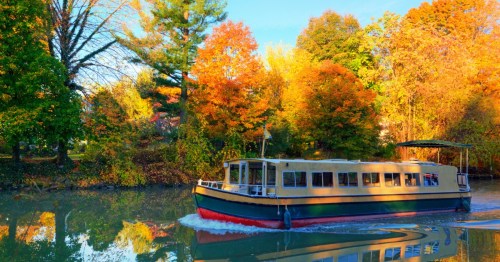 A boat glides through calm waters surrounded by vibrant autumn foliage.