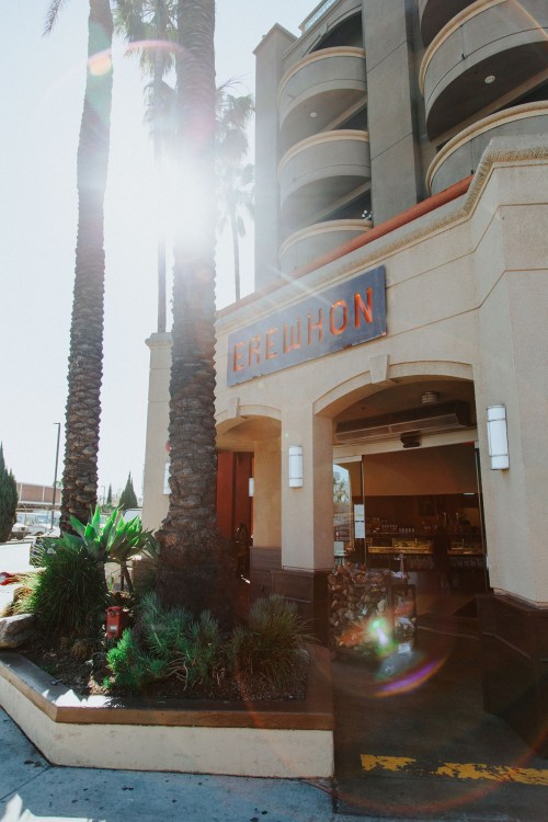 Entrance of Erewhon market with palm trees and sunlight reflecting off the building.