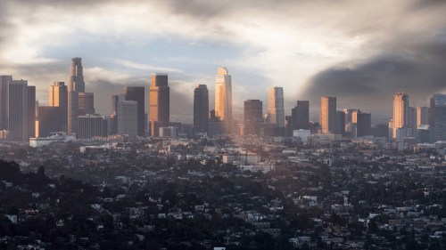 A panoramic view of a city skyline at sunset, with tall buildings and a dramatic sky filled with clouds.