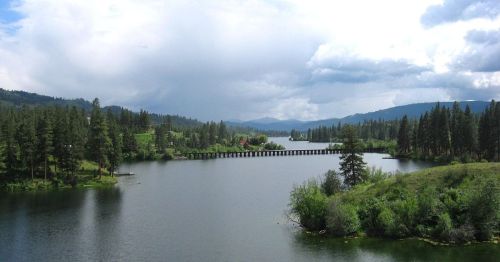 A serene landscape featuring a calm lake surrounded by lush greenery and distant mountains under a cloudy sky.