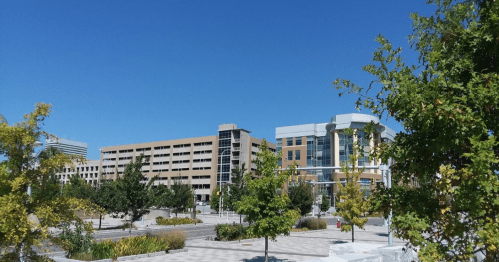 A clear blue sky over a modern urban area with buildings and trees in a landscaped plaza.