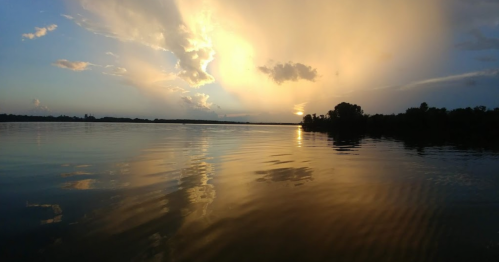A serene lake at sunset, with golden clouds reflecting on the water's surface and a calm, peaceful atmosphere.