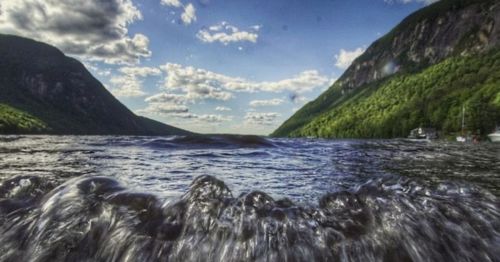 A serene view of a lake surrounded by mountains, with waves gently lapping at the shore under a cloudy sky.