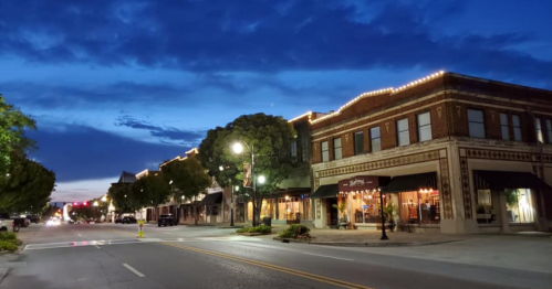 A charming downtown street at dusk, lined with historic buildings and warm lights under a blue sky.
