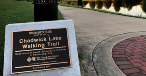 Sign for Chadwick Lake Walking Trail at Mississippi State University, with a view of the trail and lake in the background.
