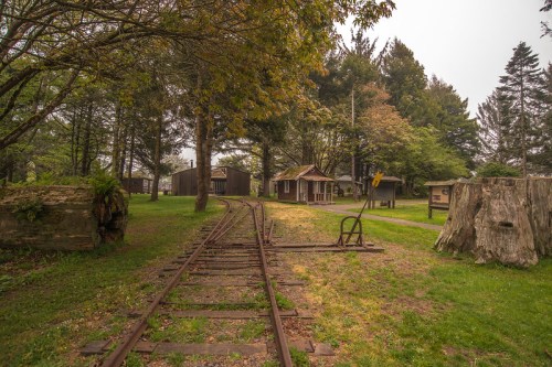 A quiet, misty scene featuring old train tracks, a small building, and trees in a lush green park.
