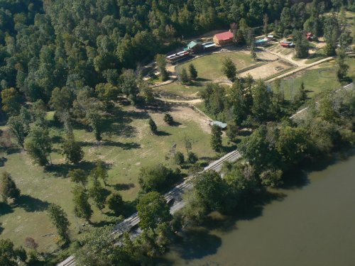 Aerial view of a green landscape with trees, a river, and a few buildings near a railway track.