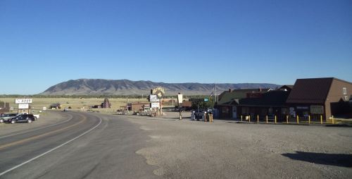 A scenic view of a rural road with buildings and mountains in the background under a clear blue sky.