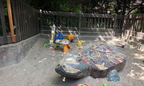 A mosaic turtle sculpture in a sandy play area with colorful toys scattered around.