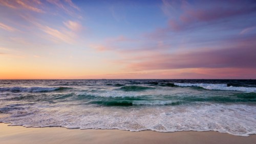 A serene beach scene at sunset, with gentle waves lapping at the shore under a colorful sky.