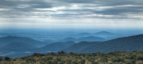 A panoramic view of rolling hills under a cloudy sky, with layers of mountains fading into the distance.